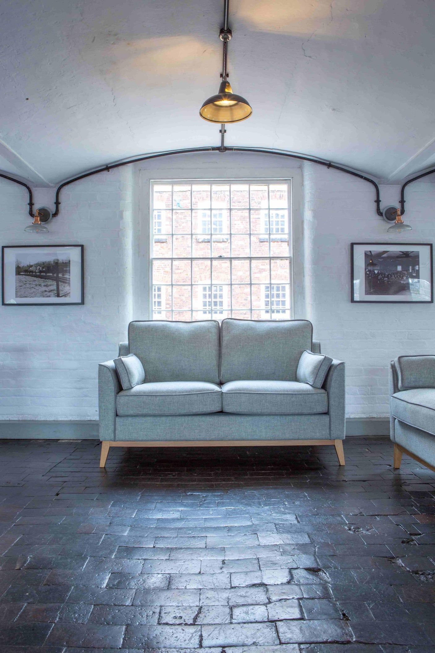 Light grey fabric sofa with wooden legs in a bright living room with brick flooring