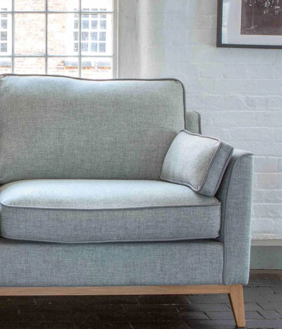 Light grey fabric sofa with wooden legs and cushion in bright living room