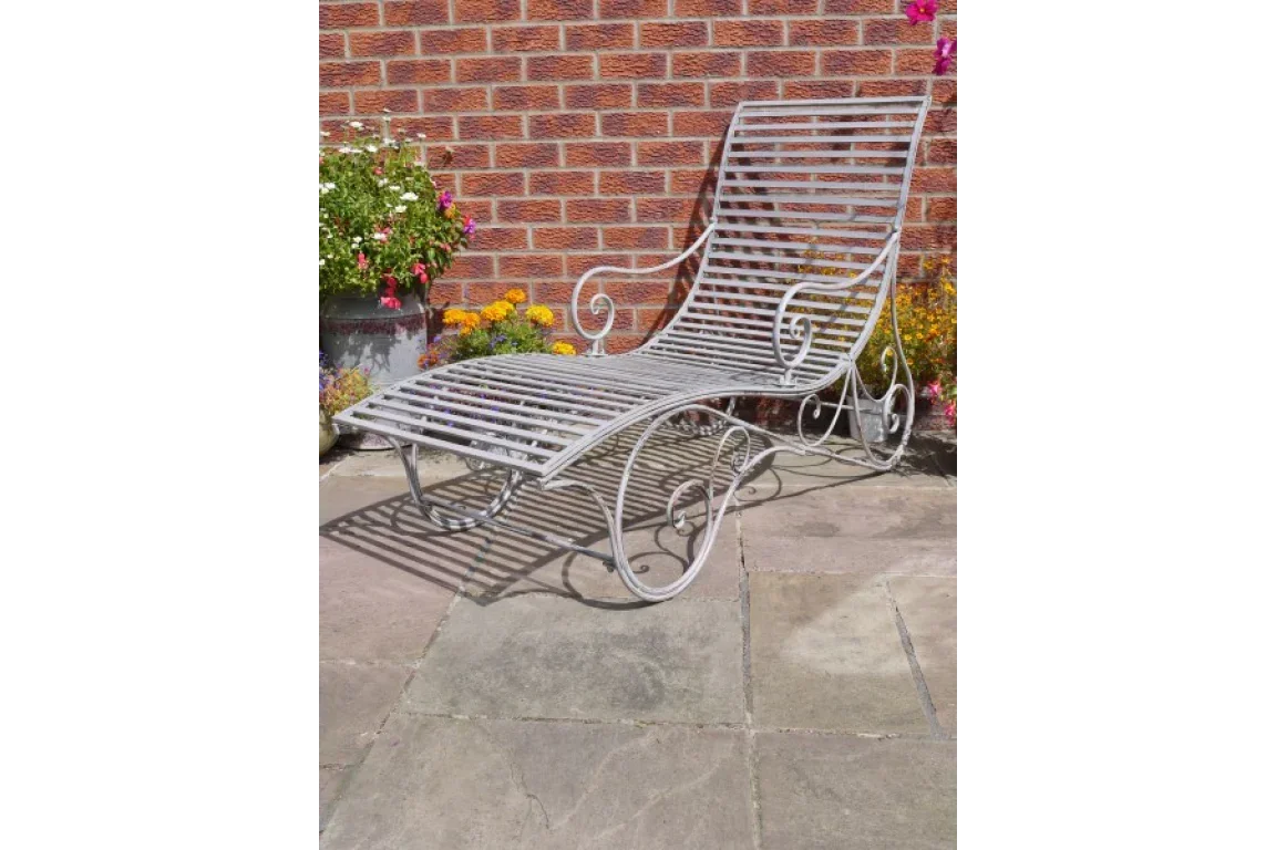 Metal garden lounge chair with slatted design on patio near brick wall and flowers