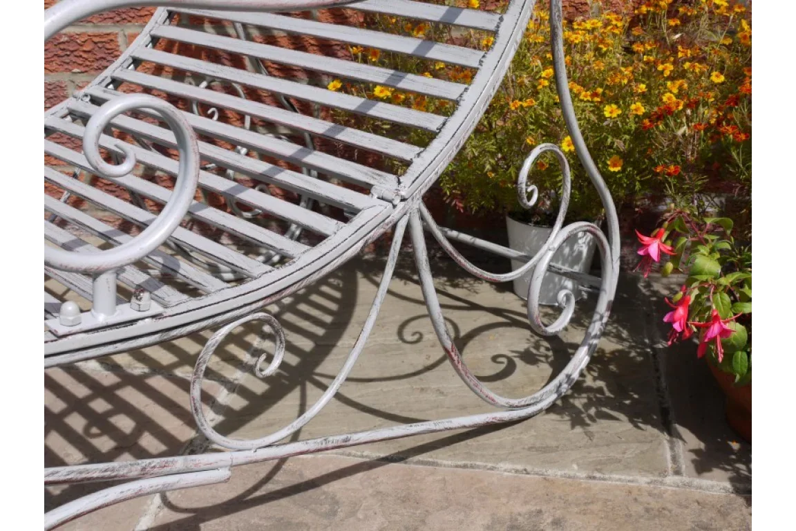Metal garden bench with scroll design on stone patio beside flowering plants