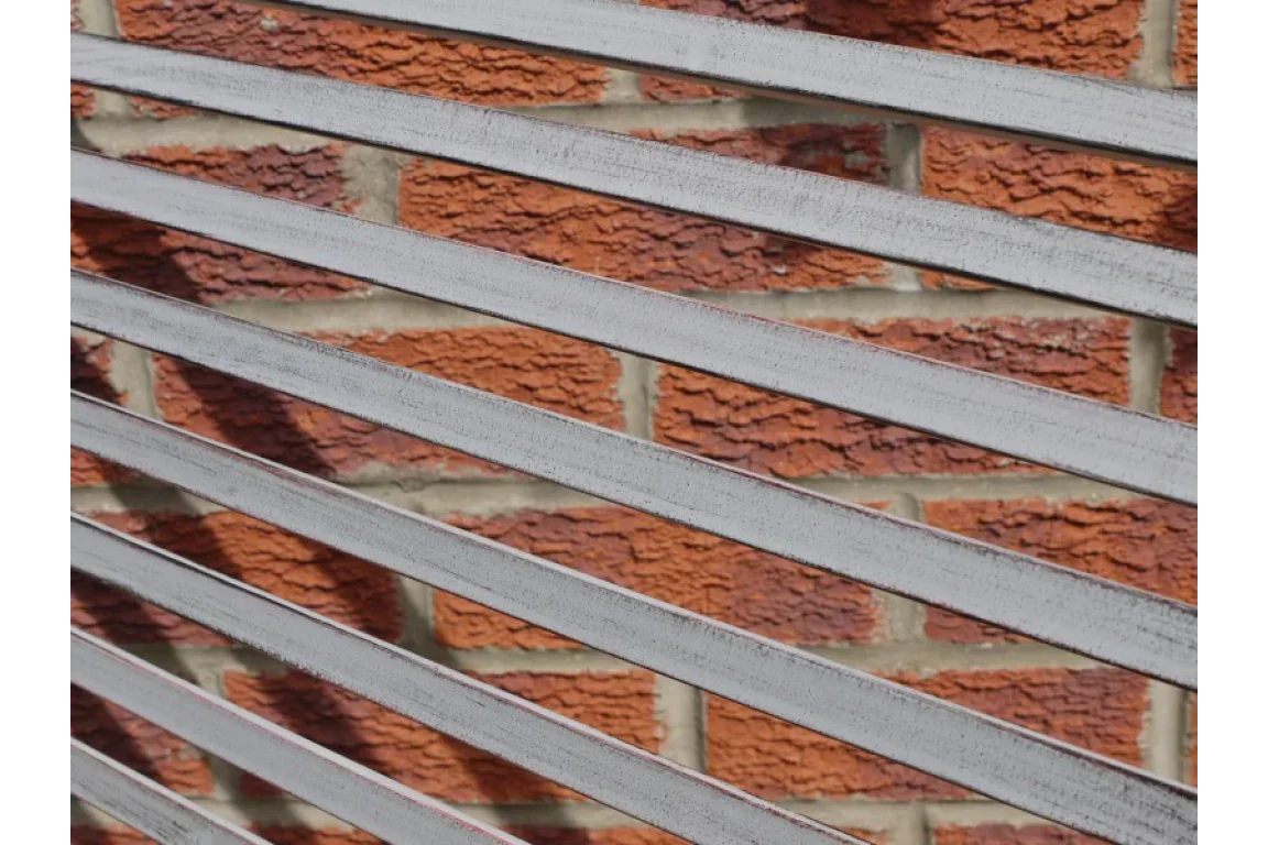 Closeup of silver metal garden fence slats with red brick wall background