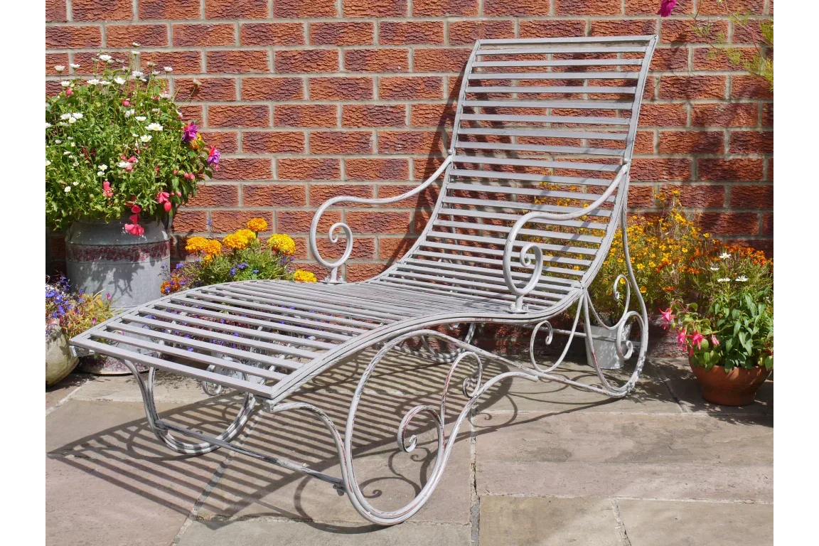 Metal garden lounger with curved frame and slatted seat on stone patio beside flowers