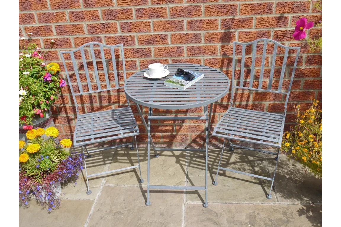 Metal bistro table and chairs set on patio with cup, book, and plants against brick wall