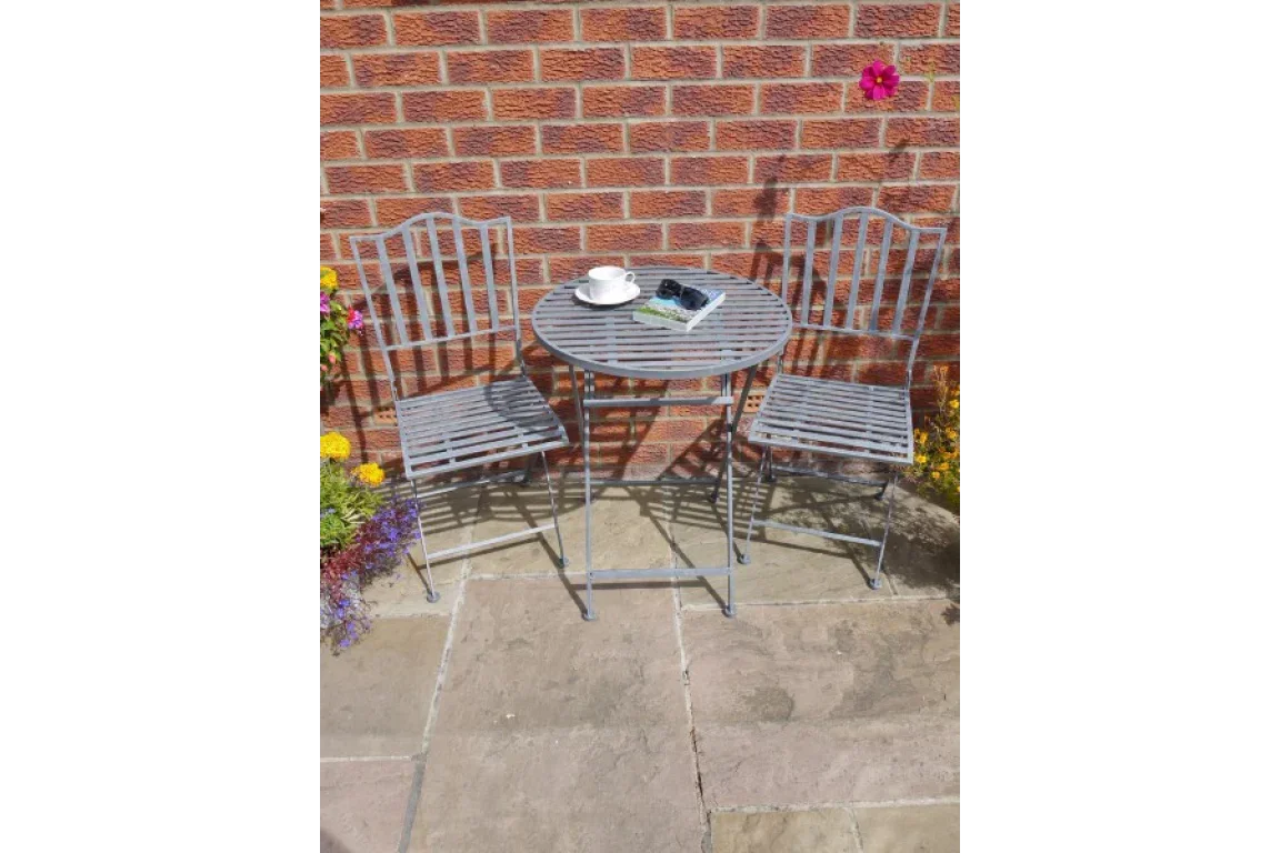Metal patio bistro set with two chairs and round table on stone paving against brick wall