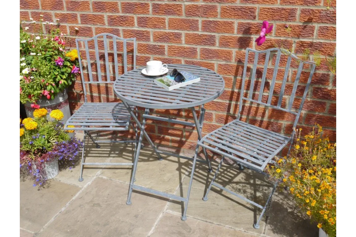 Metal bistro set with two chairs and round slatted table on patio beside flowers