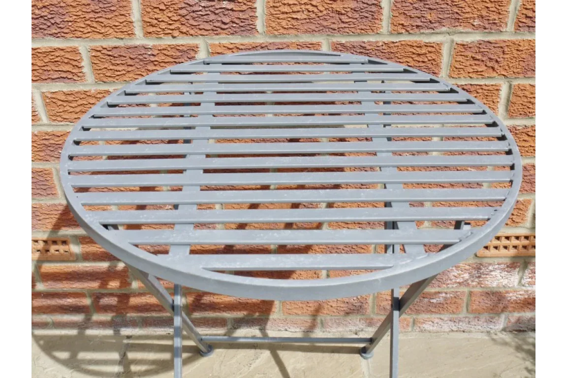 Grey metal slatted outdoor table with folding legs against brick wall