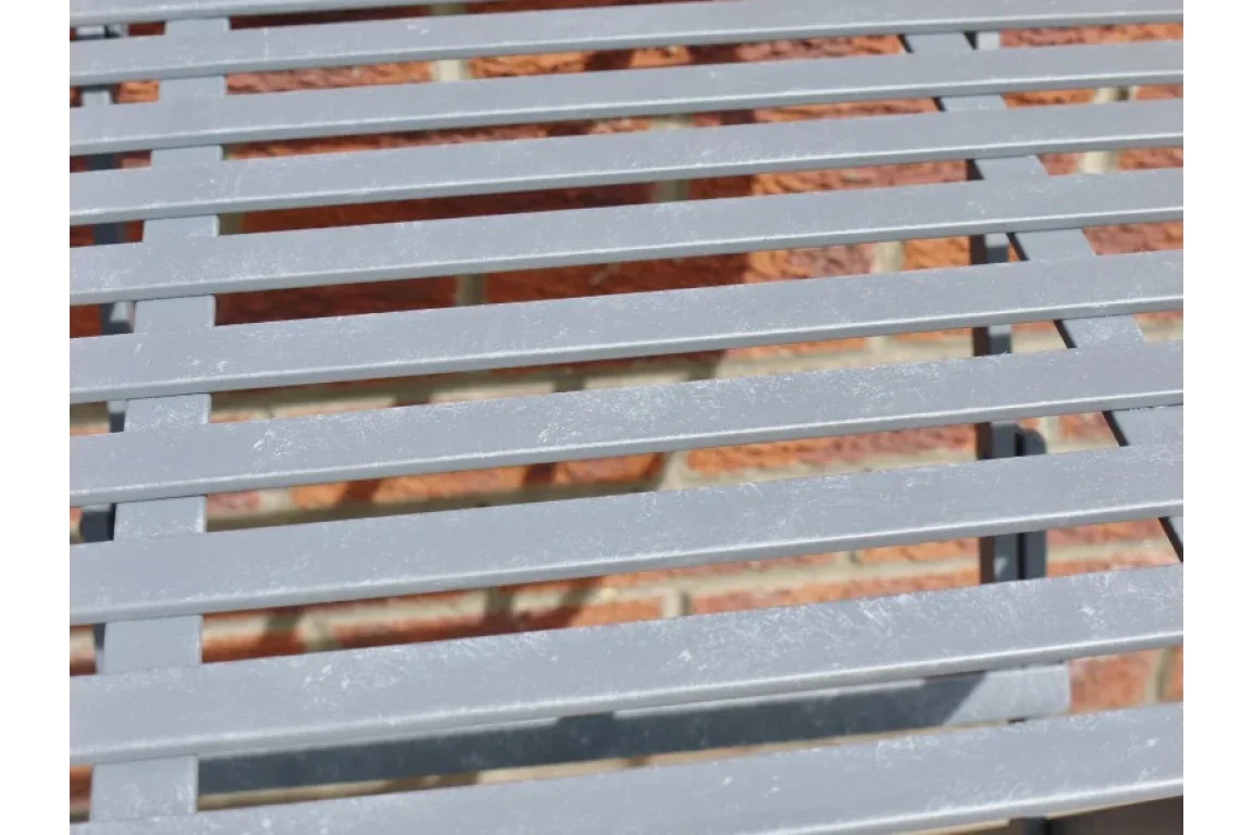 Grey metal outdoor bench slat detail with brick wall background