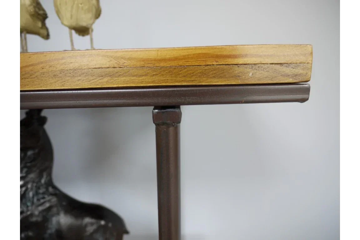 Close-up of wooden tabletop with metal legs and partial decorative bird sculptures