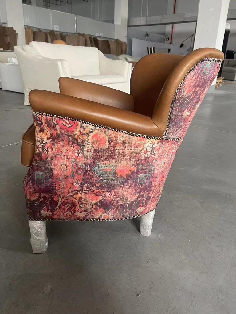 Brown leather armchair with floral patterned fabric back and nailhead trim, side view