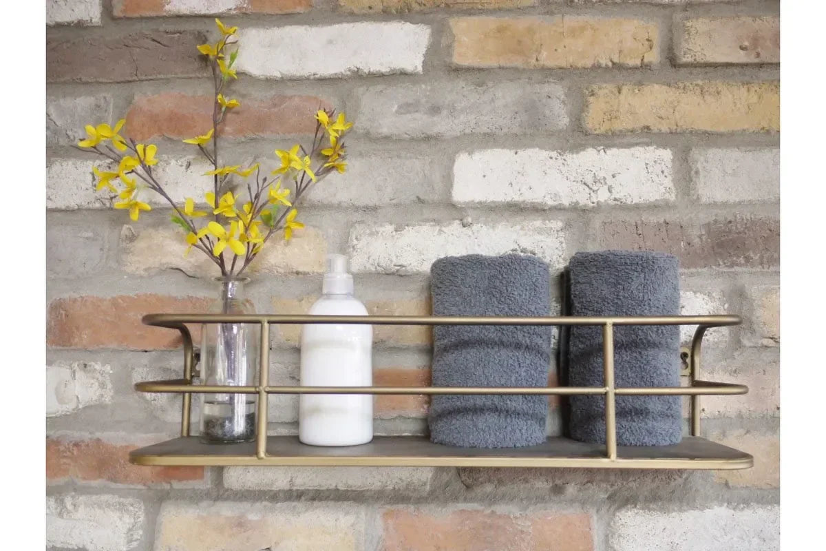 Wall shelf with gold metal rail holding rolled grey towels, soap dispenser, glass vase with yellow flowers