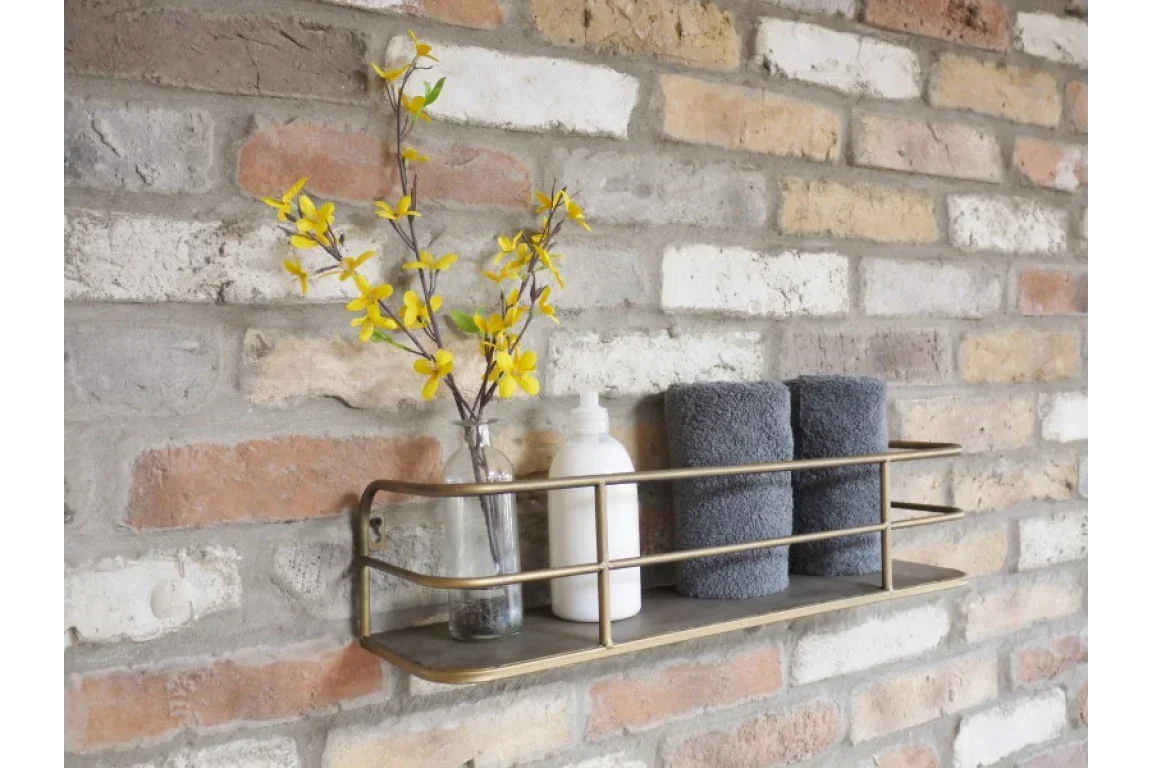 Wall mounted brass shelf with two grey towels, glass vase with yellow flowers, and soap dispenser