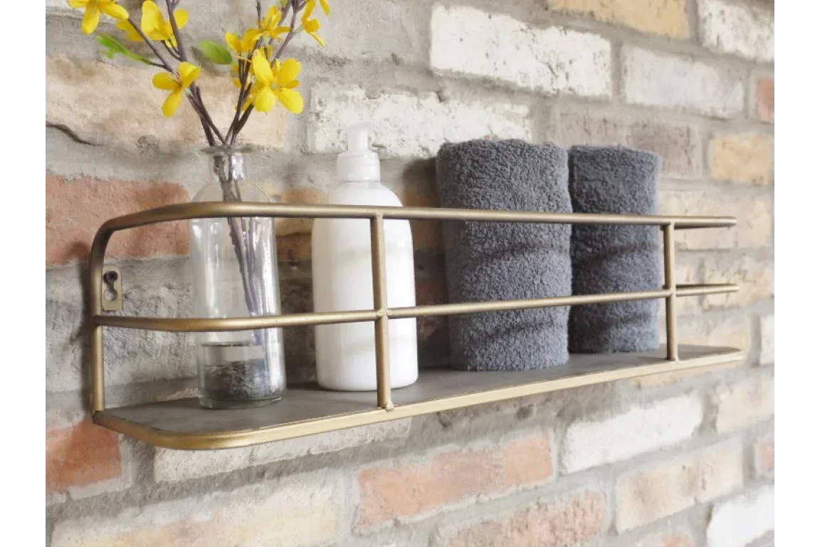 Wall mounted brass bathroom shelf with rolled grey towels, lotion bottle and vase with flowers
