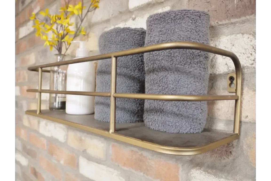Wall-mounted brass bathroom shelf with grey towels, vase, and soap dispenser