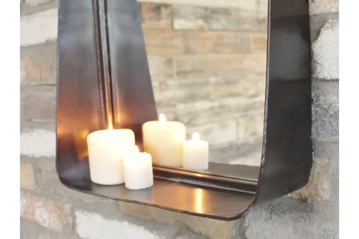 Wall mirror shelf with black metal frame holding lit pillar candles against brick wall