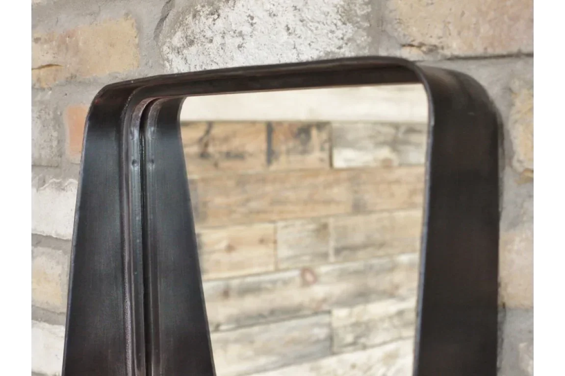 Black metal frame wall mirror with rounded edge against exposed brick background