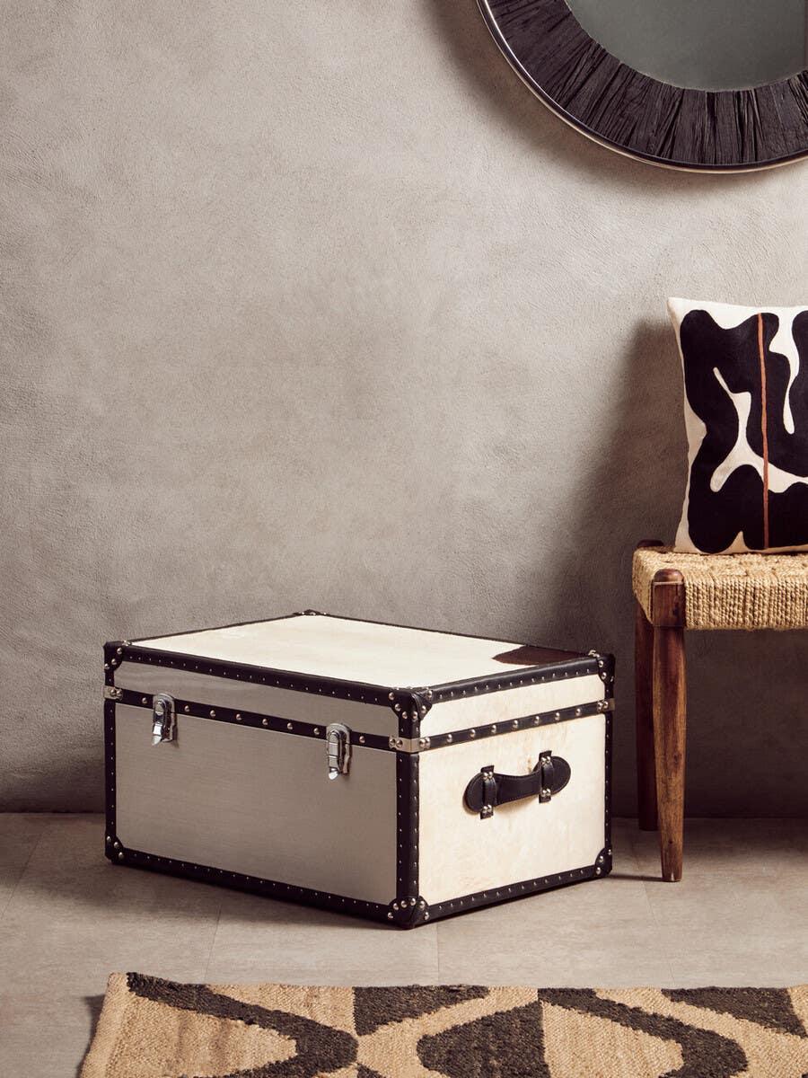 Cream and black storage trunk with metal clasps beside bench and monochrome cushion