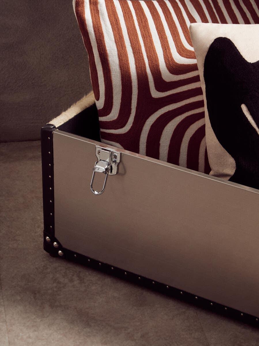 Beige metal storage trunk with chrome latch and patterned cushions inside