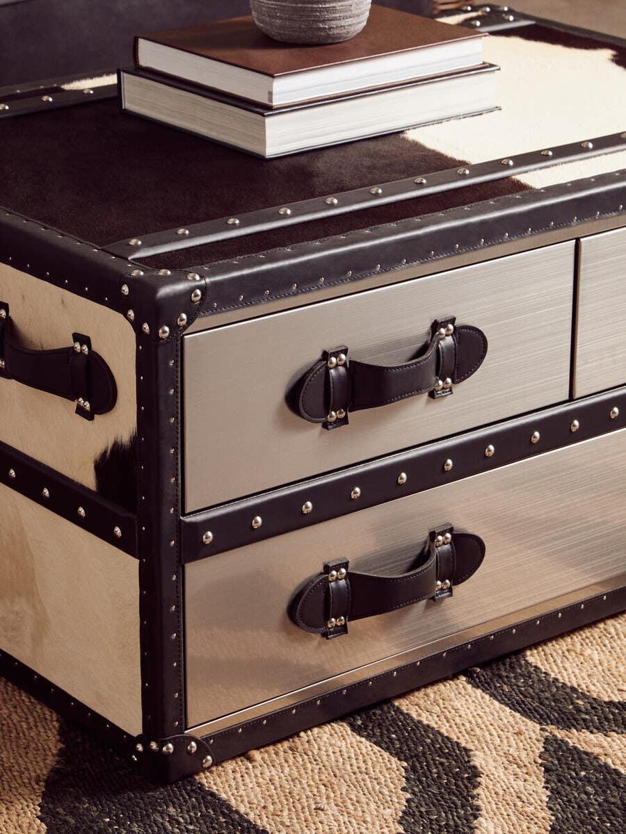 Metal trunk coffee table with black leather handles and studded edging on patterned rug
