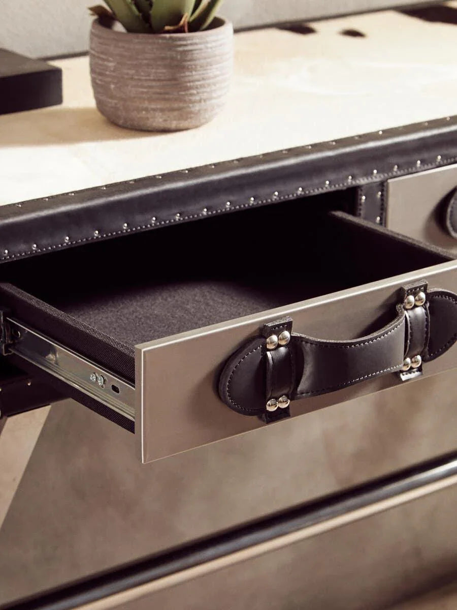 Closeup of metal drawer with black leather handle on modern desk, potted plant on top