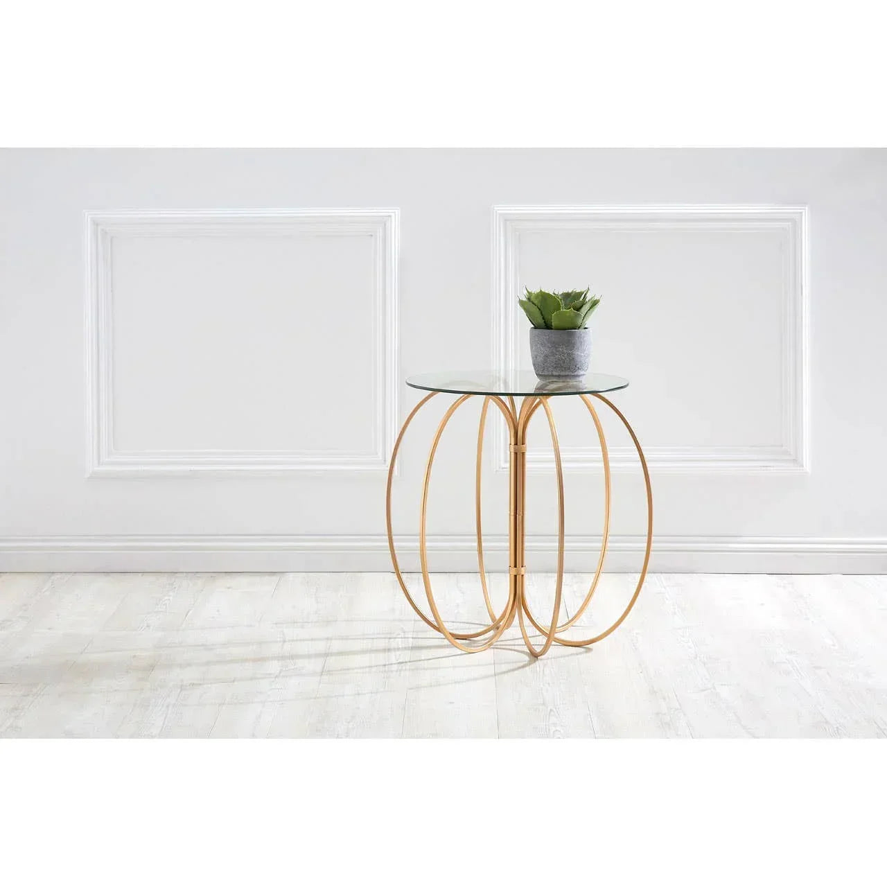 Glass top side table with gold metal frame and potted plant, set against a white wall
