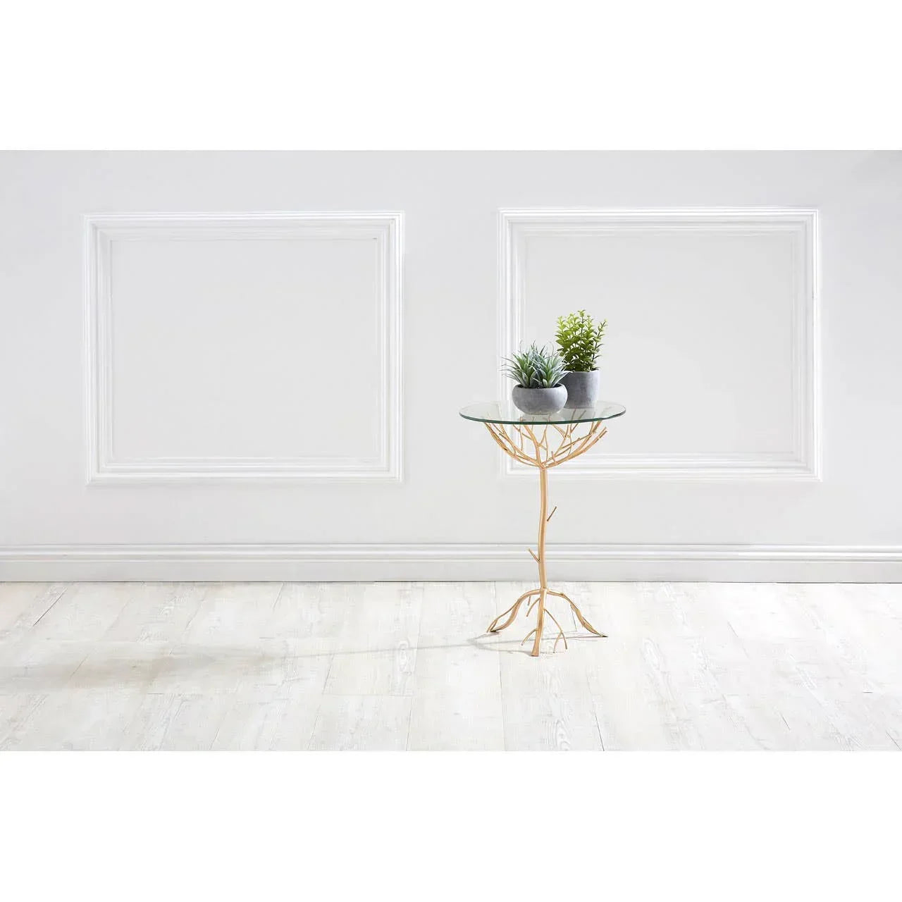 Glass side table with gold branch base and two potted plants against white paneled wall