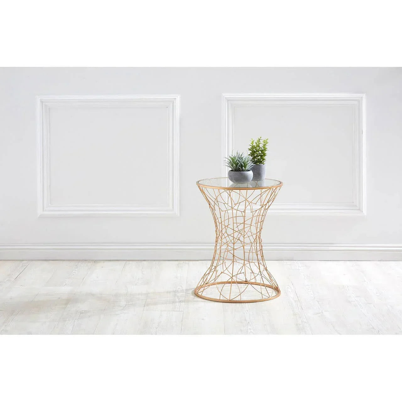 Round glass top side table with gold wire frame and two small potted plants in modern room
