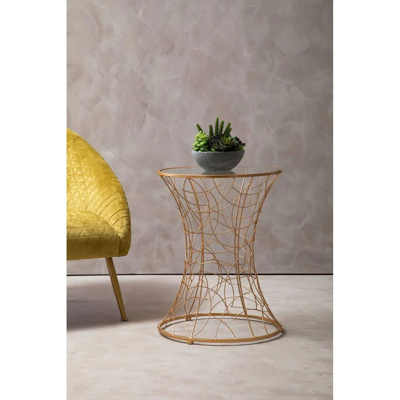 Gold wire side table with glass top and potted succulents beside yellow velvet chair
