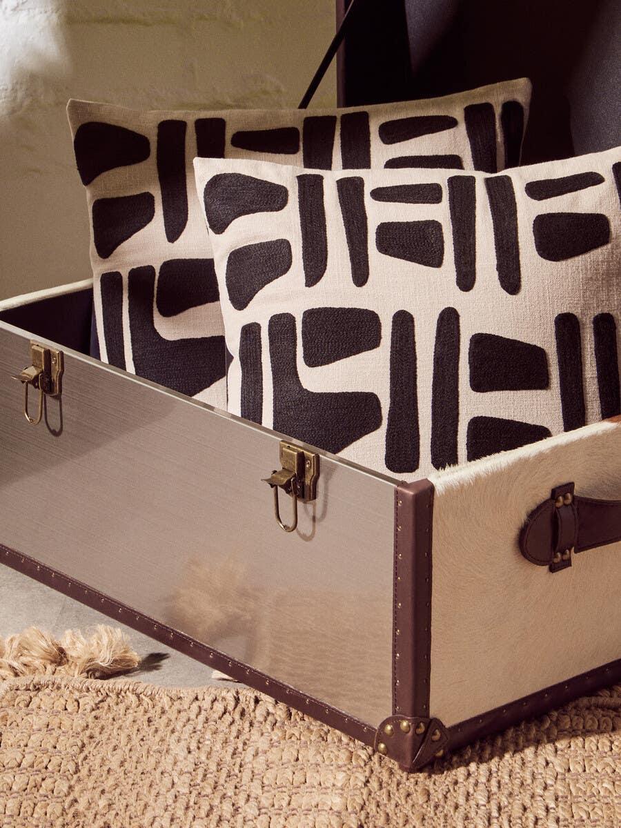 Geometric black and cream cushions placed inside a decorative storage trunk on woven rug