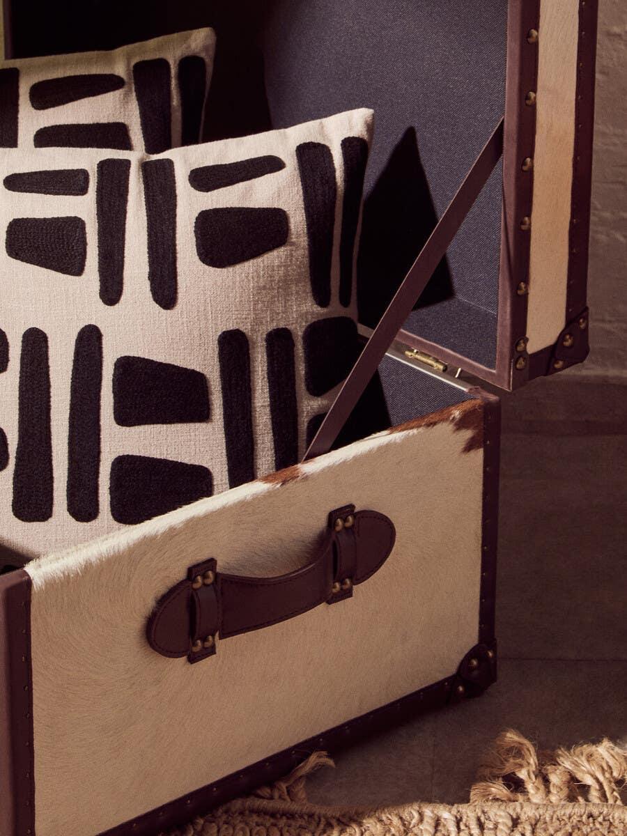 Two patterned black and cream cushions in a cowhide storage trunk on a textured rug