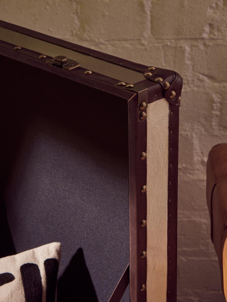 Close-up of leather-trimmed storage trunk with metal rivets and fabric cushion