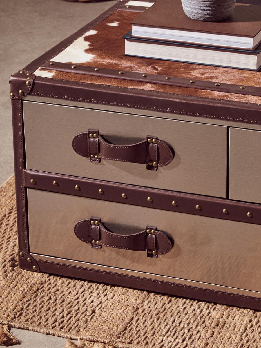 Brown leather storage trunk coffee table with metal rivets and cowhide top on woven rug