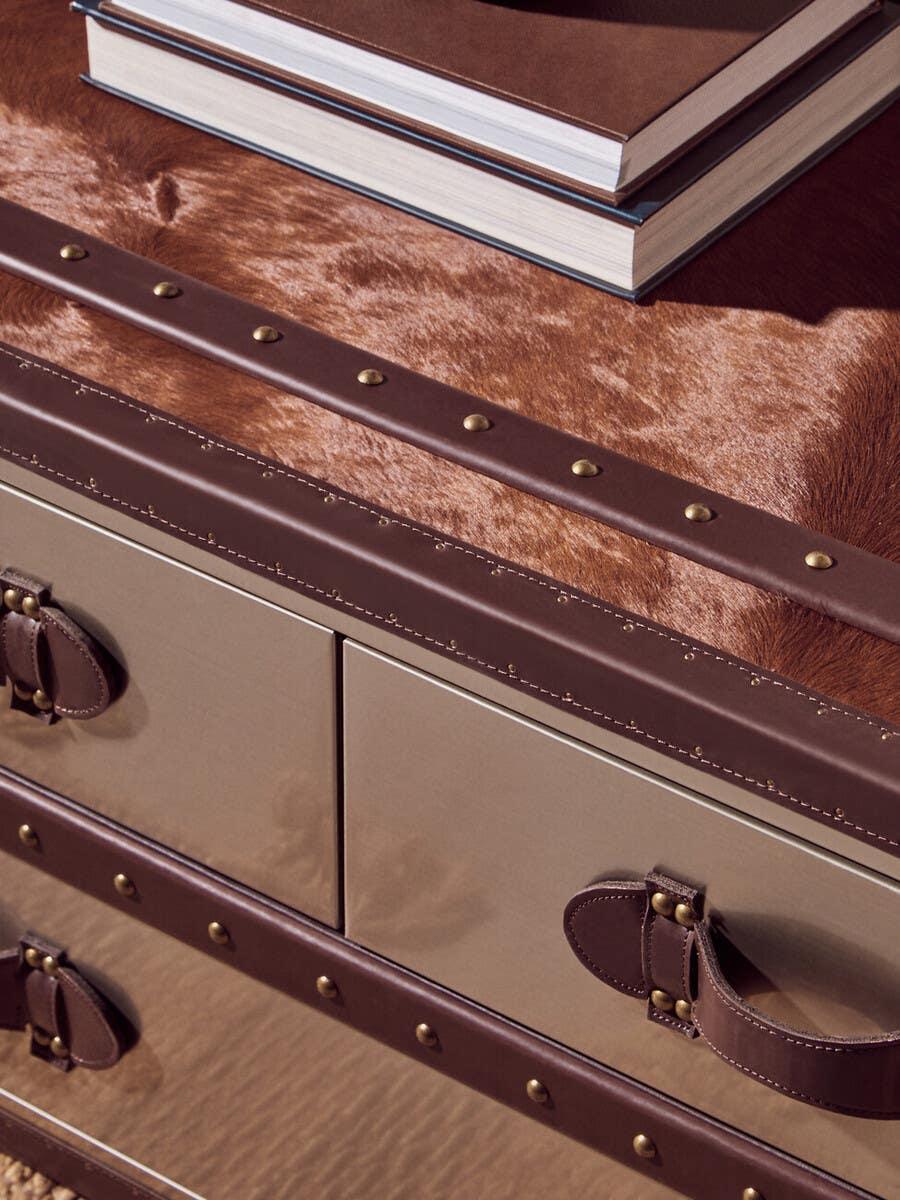 Leather trim storage chest with brass rivets and faux fur top, stacked books displayed