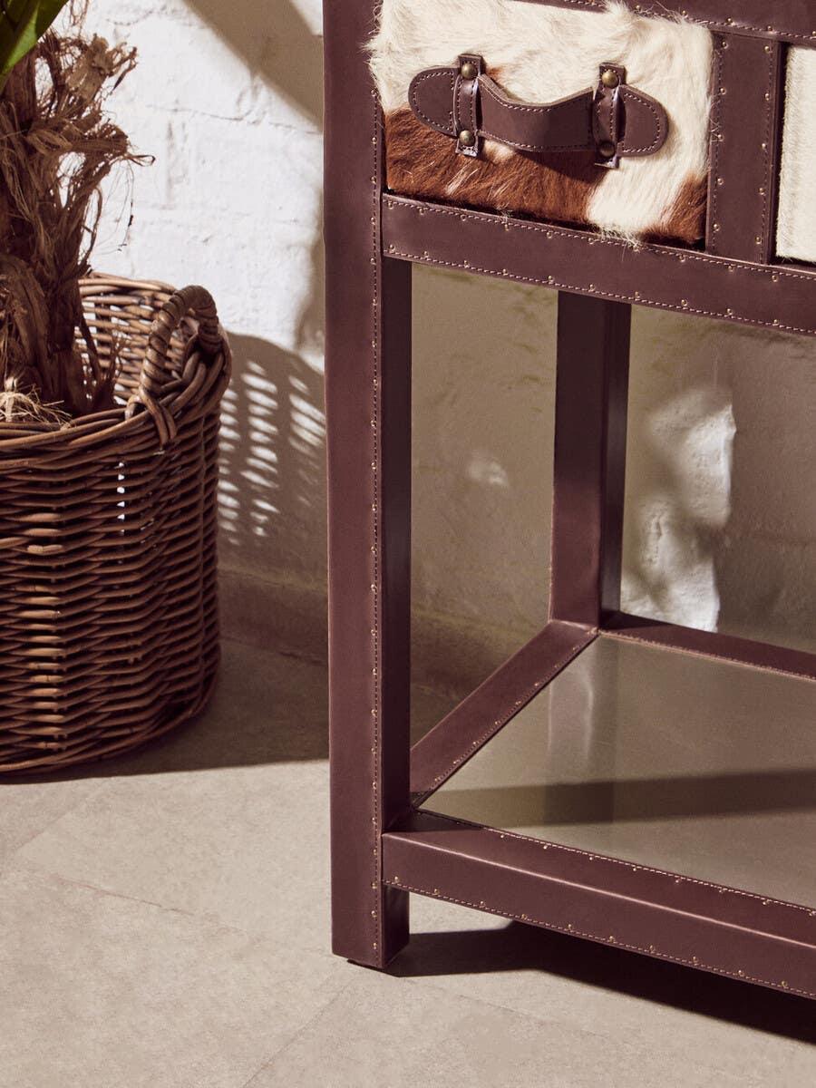 Brown leather and cowhide storage unit drawer with metal accents beside wicker basket