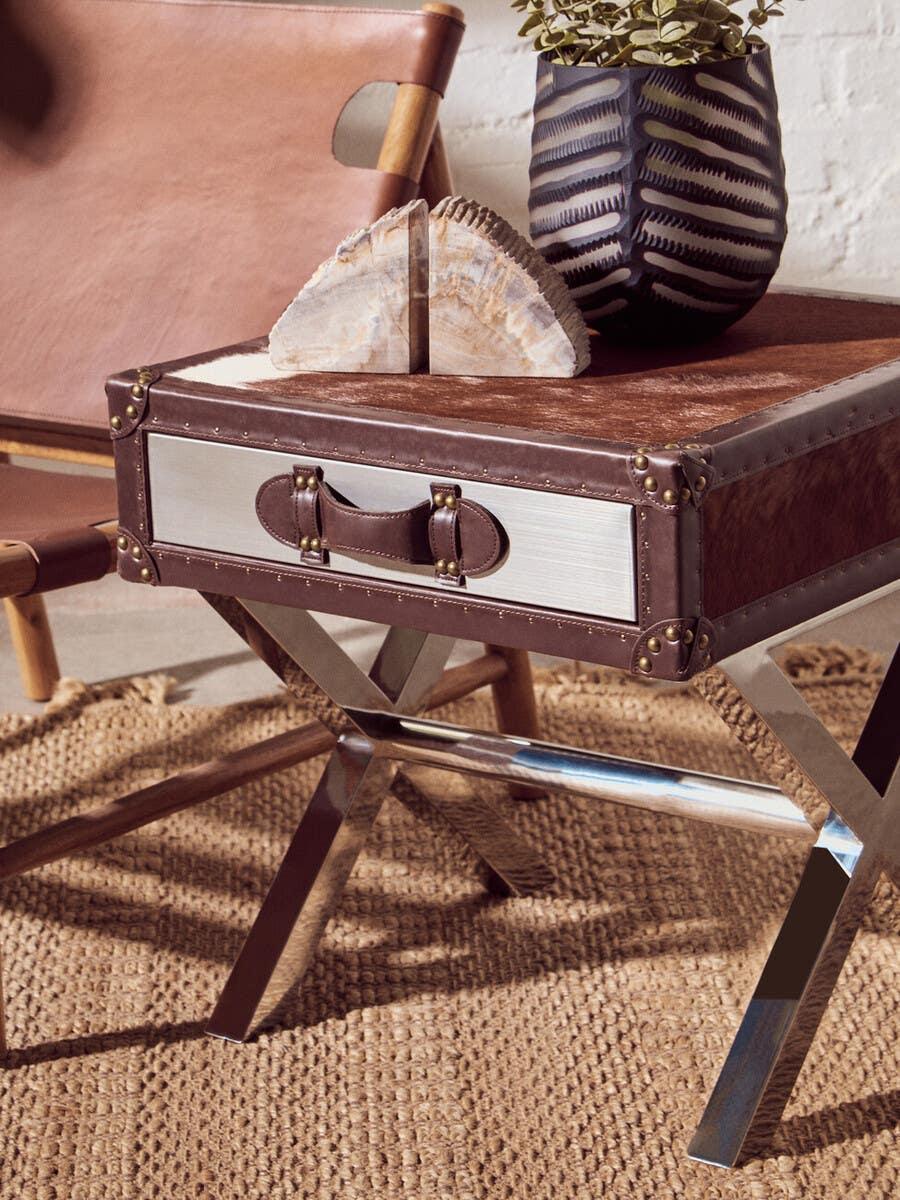 Brown leather side table with chrome legs, woven rug, and ceramic vase with plant