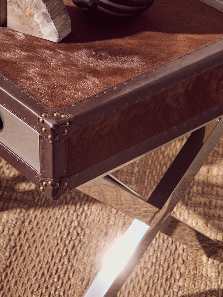 Brown leather coffee table with metal corners and crossed metal legs on woven rug