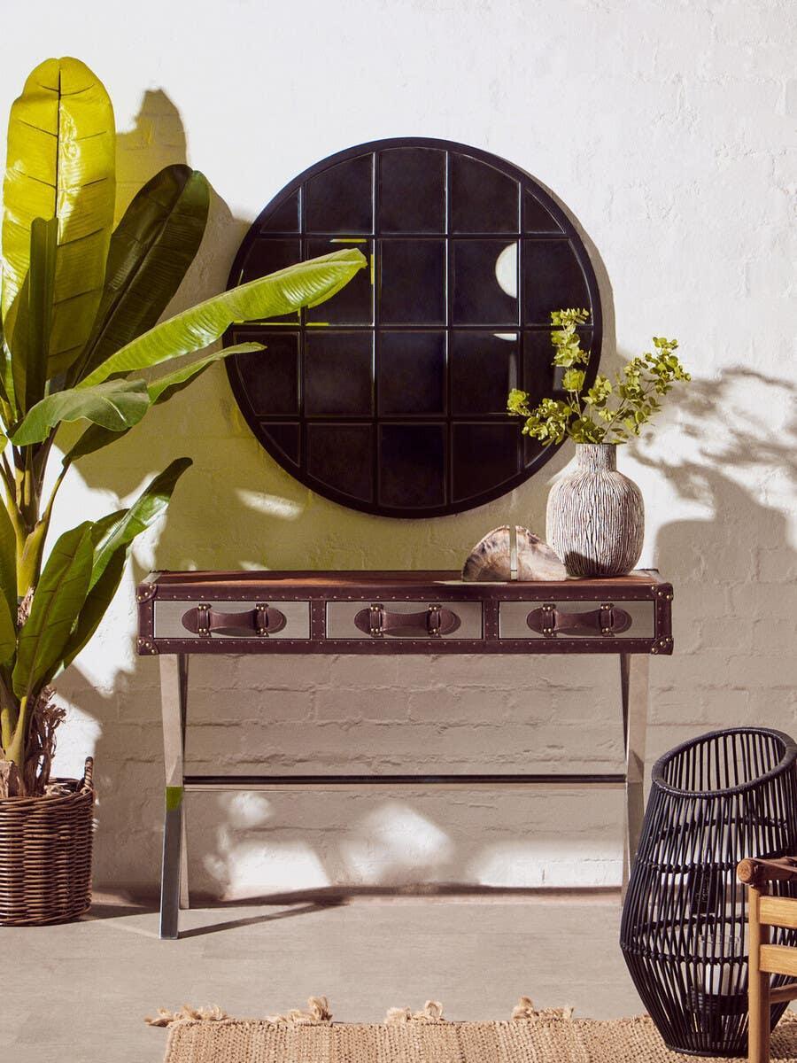 Three drawer console table with metal legs under round mirror, styled with decor accents