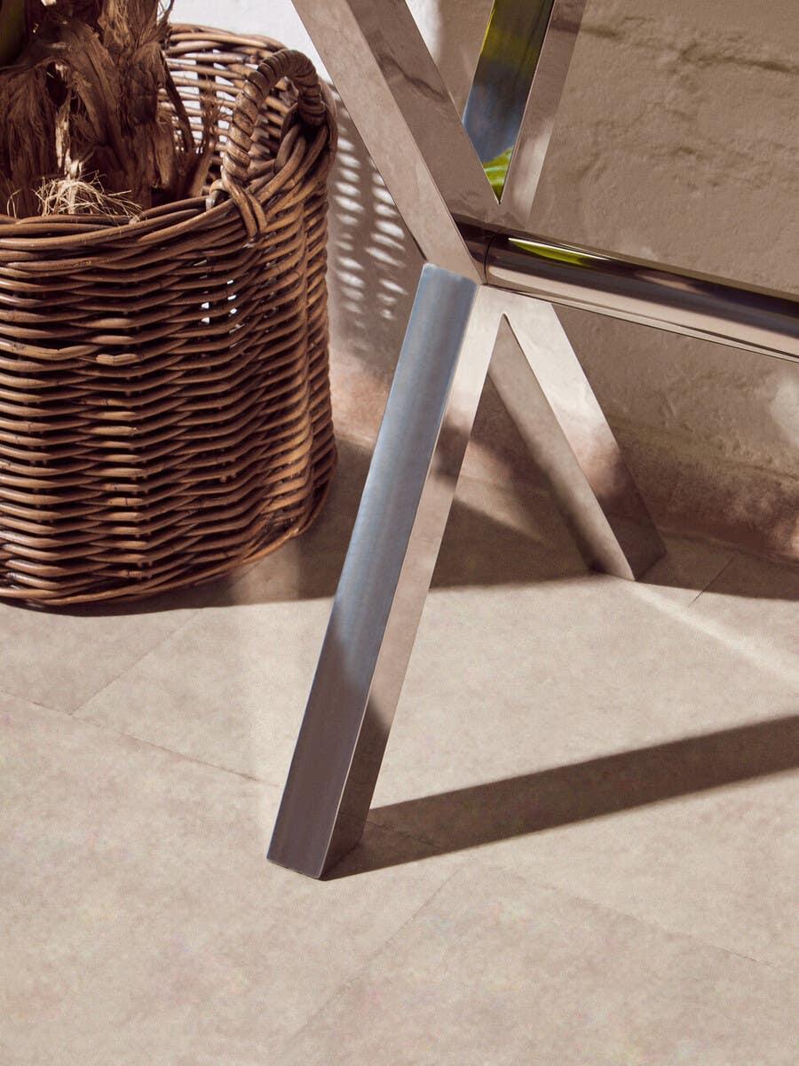 Close-up of chrome dining table leg beside woven rattan basket on tiled floor