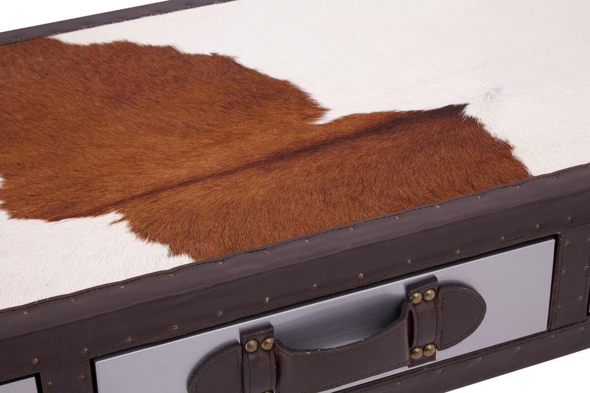 Closeup of cowhide trunk with brown and white hide top, leather trim, and metal drawer handle