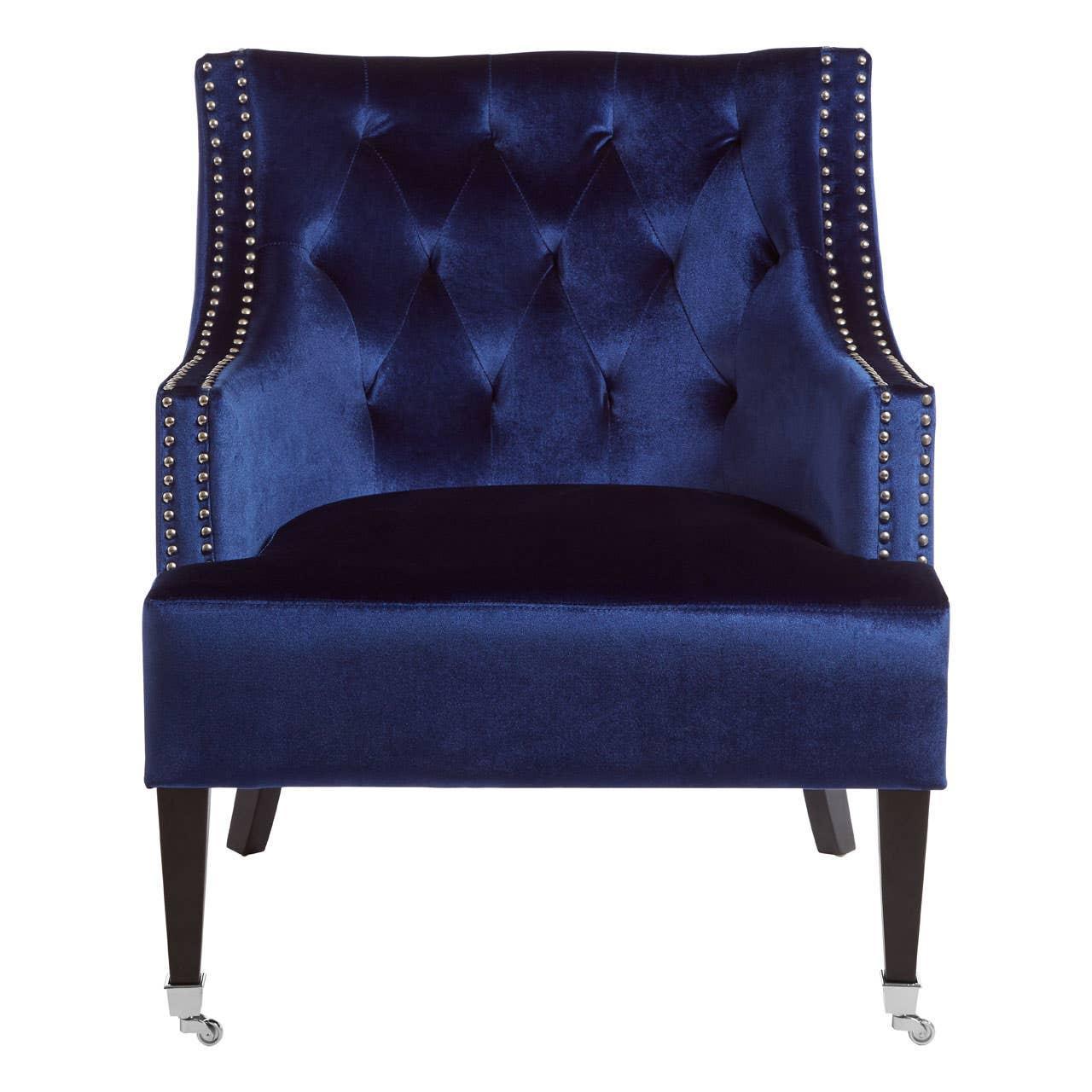Blue velvet accent chair with button-tufted back, studded trim, dark legs and front castors