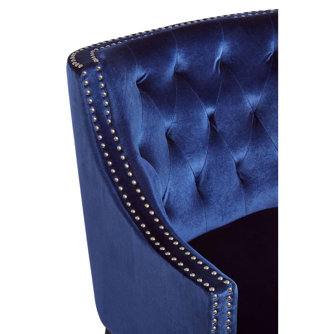 Blue velvet armchair with button tufting and silver stud detailing on curved backrest
