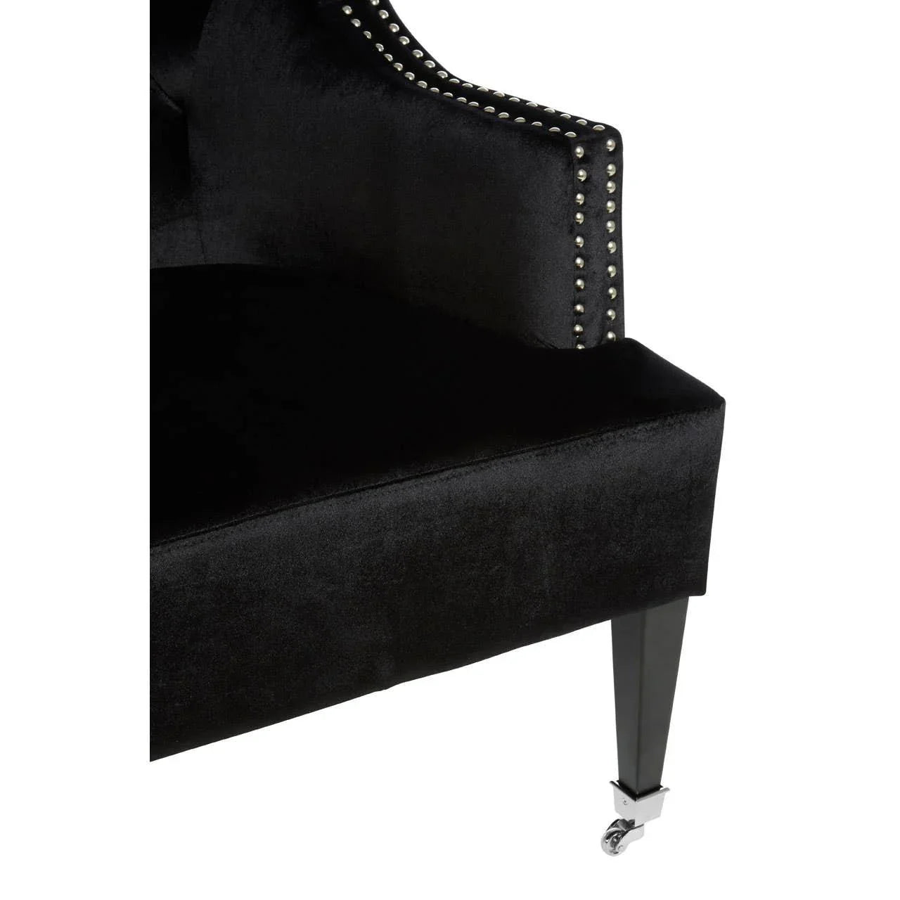 Black velvet chair with studded trim and chrome caster leg, close-up angle