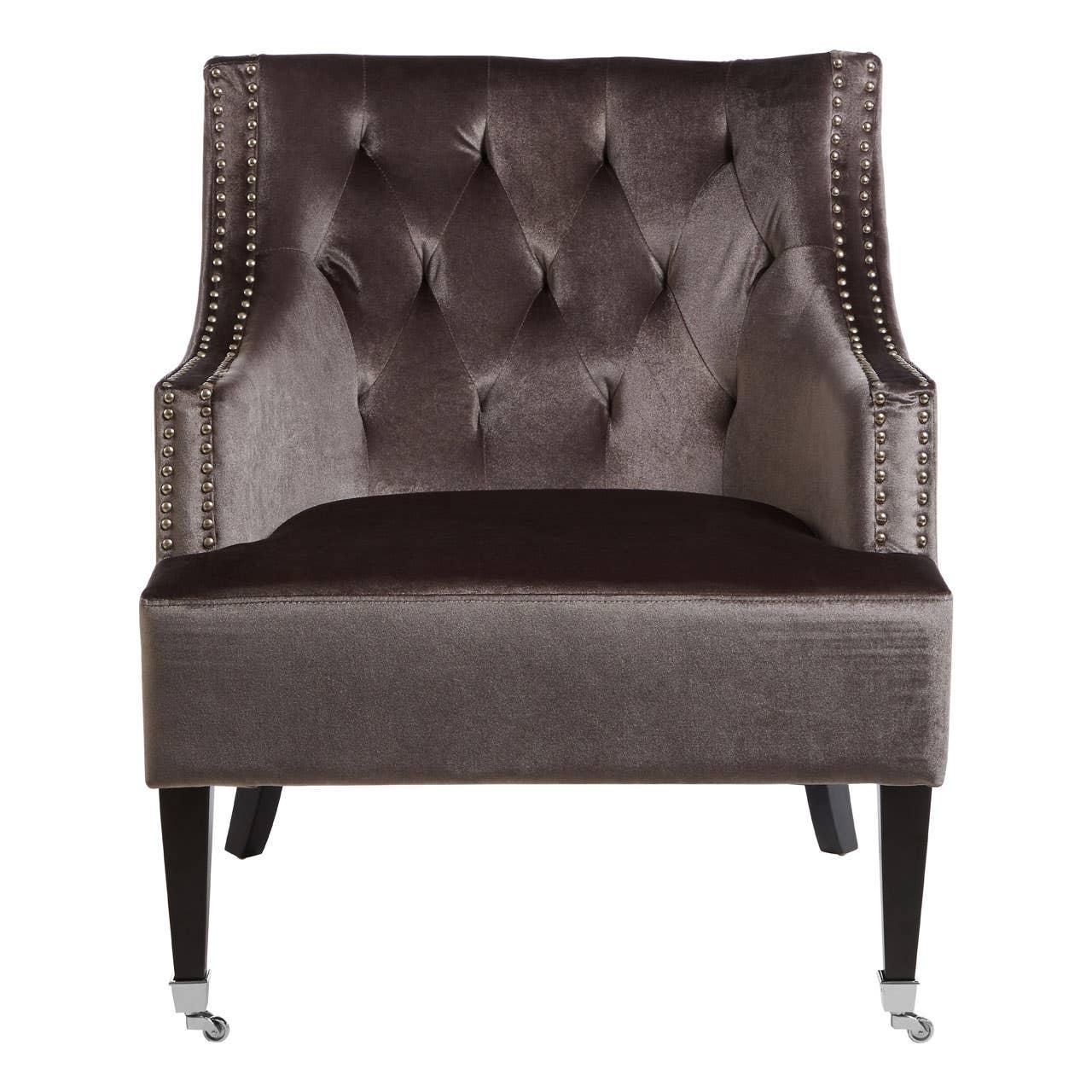 Velvet accent chair with button tufted back, studded trim, and dark wood legs on castors