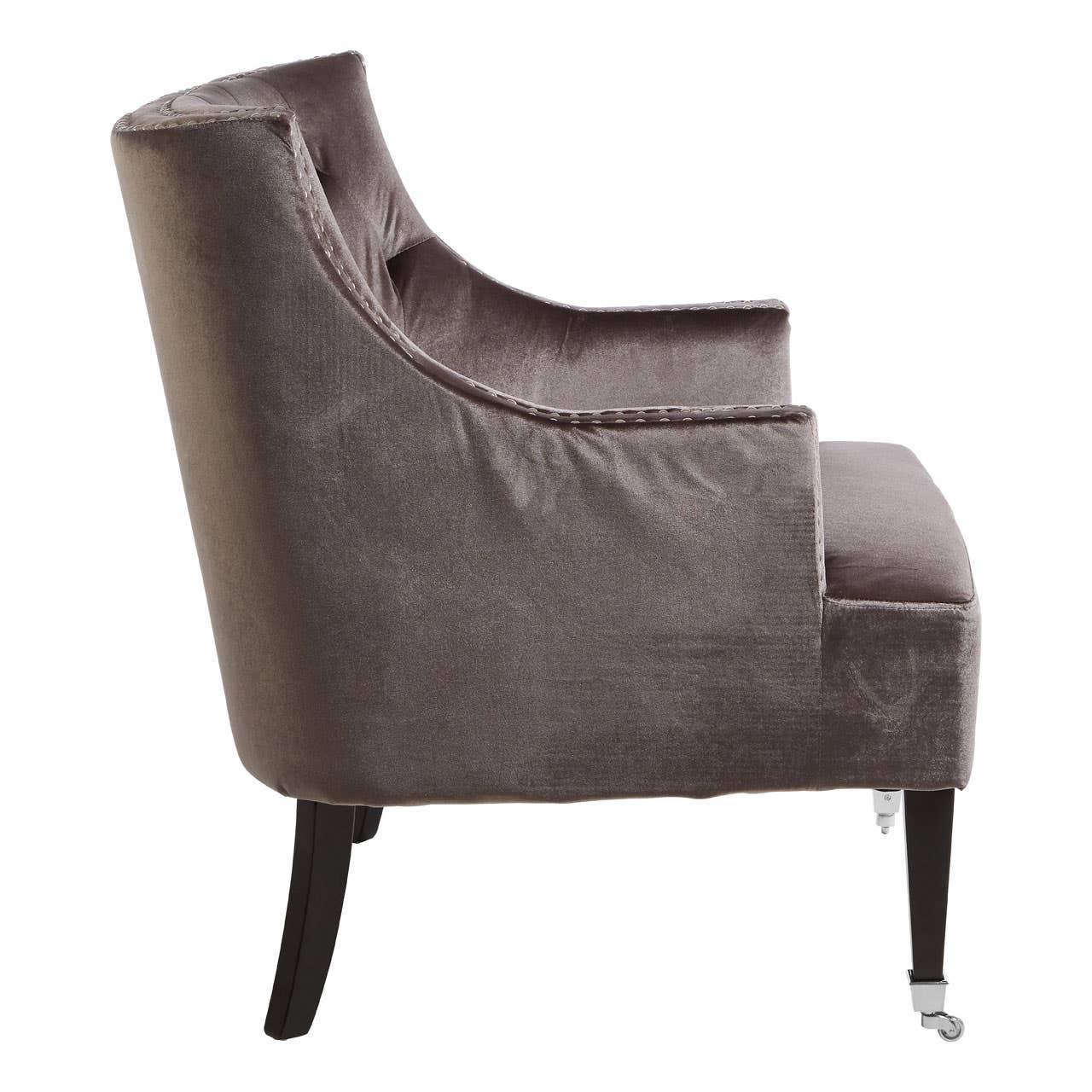 Side view of velvet armchair with dark wooden legs and front castor wheels