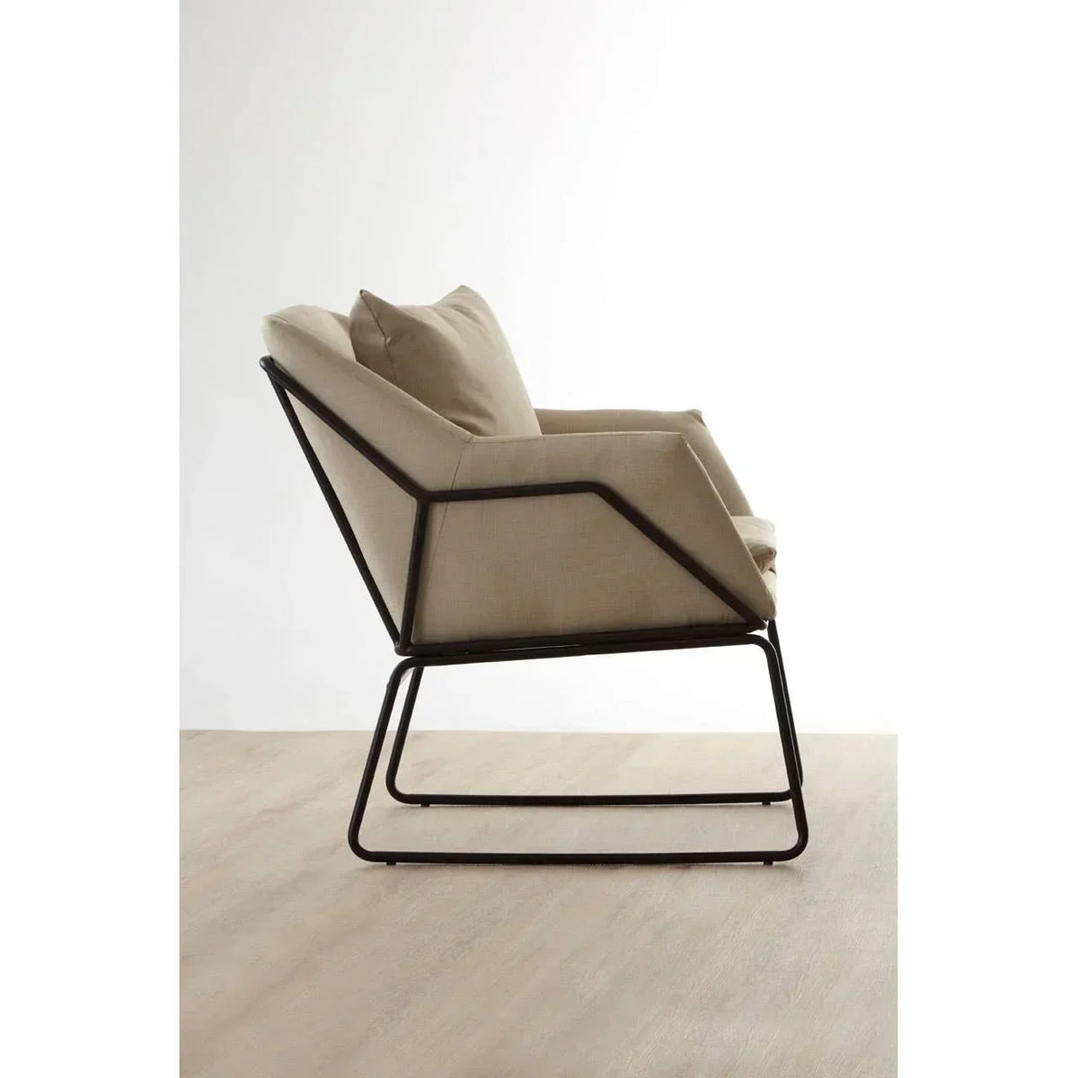 Beige armchair with metal frame and angled legs on light wood floor, side profile view