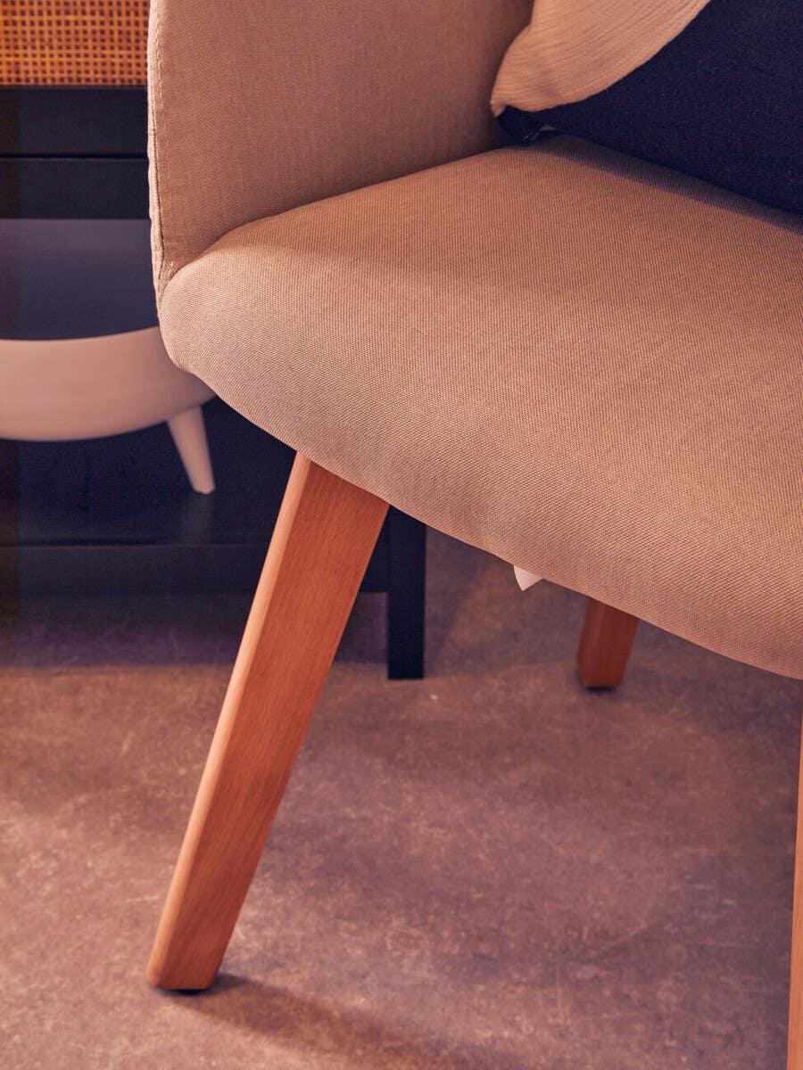 Beige upholstered dining chair with wooden legs closeup on textured floor