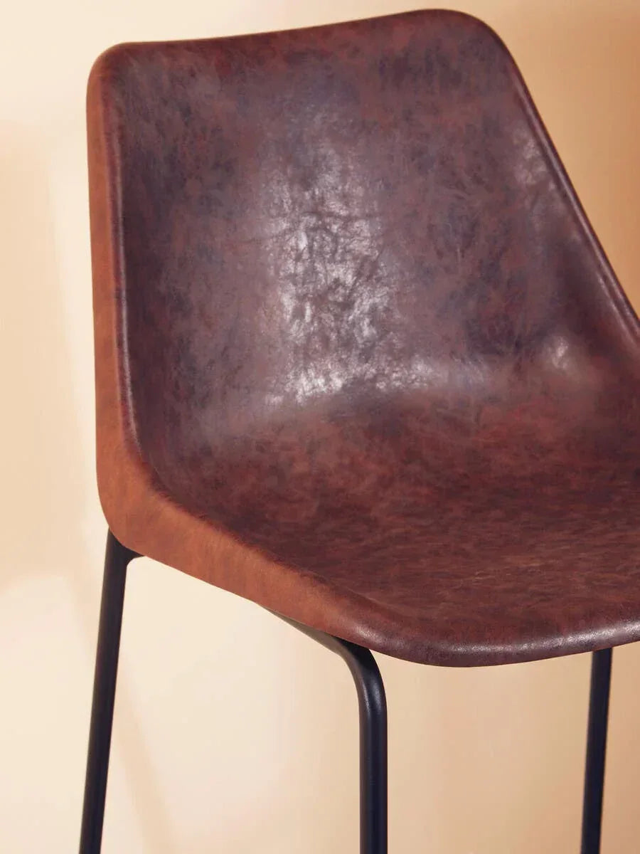 Brown faux leather bar stool with black metal legs against beige background