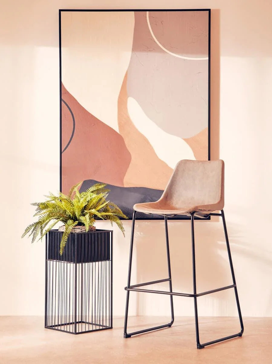 Modern bar stool with beige seat and black legs beside metal plant stand and abstract wall art
