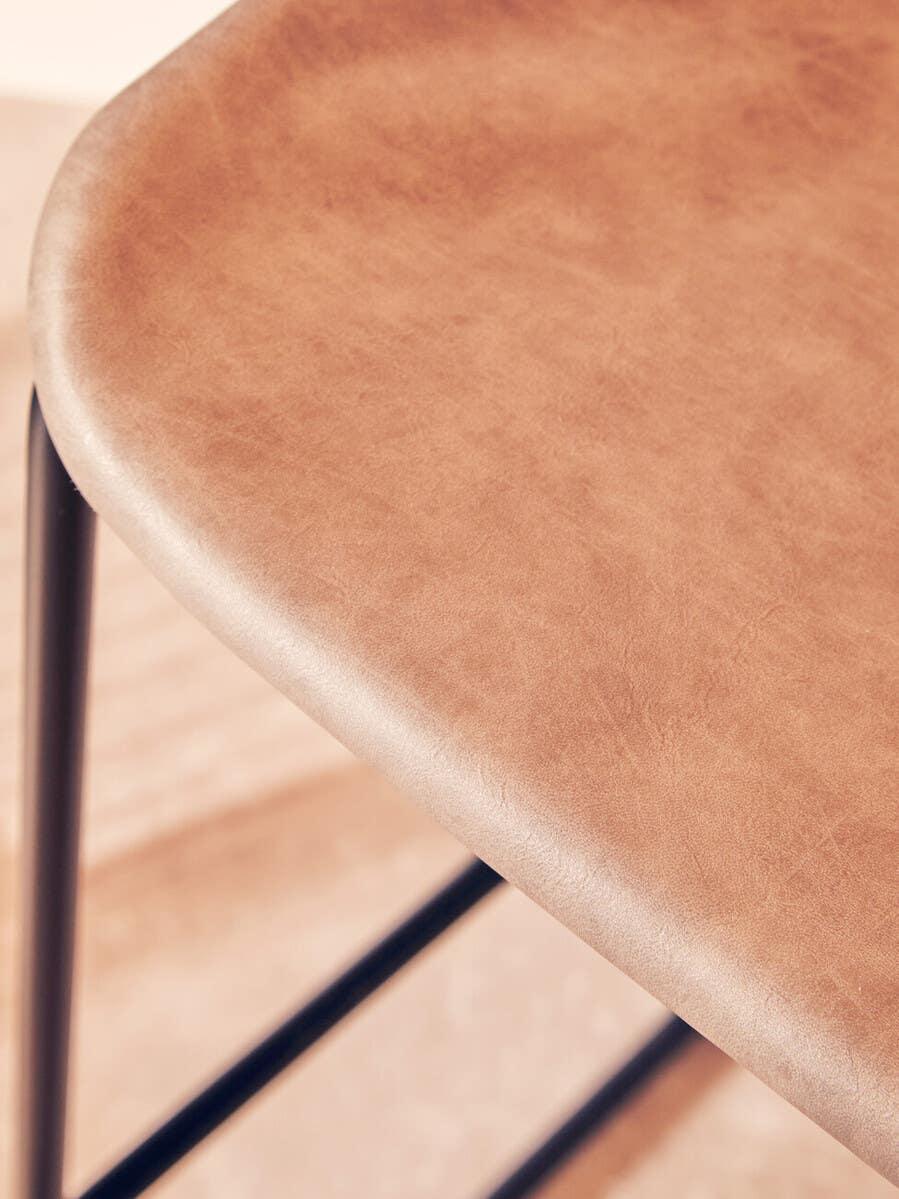 Light brown faux leather bar stool seat with black metal legs close-up