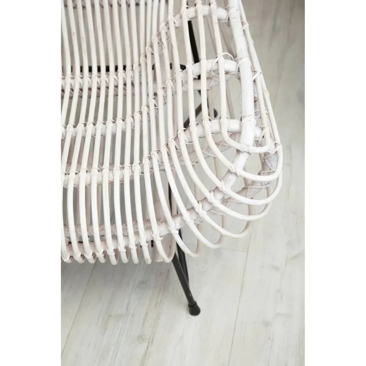 Closeup of white rattan chair seat and arm detail with black metal legs on light wood floor