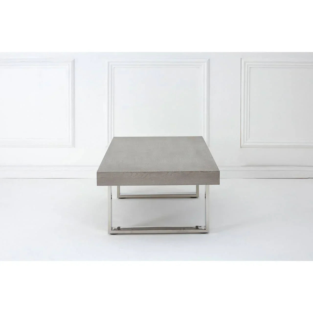 Rectangular grey wood coffee table with chrome metal legs against white paneled wall